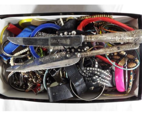 An unsorted box of costume jewellery, including a silver handled cake knife and cake server, hallmarks unclear.