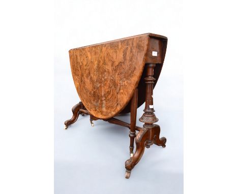 A Victorian walnut-veneered oval drop leaf table with gate legs and ornate carved supports, standing on castors, some lifting