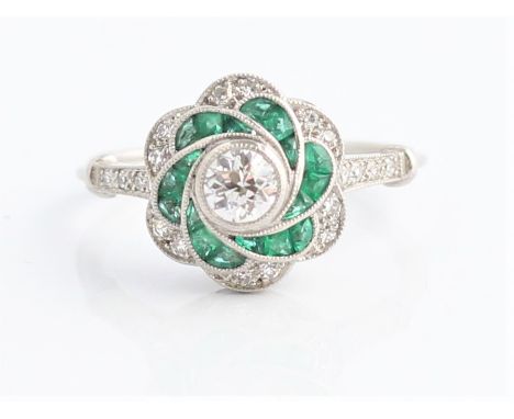 An emerald and diamond flower design dress ring, set with a central round brilliant cut diamond, measuring approx. 0.30ct, su