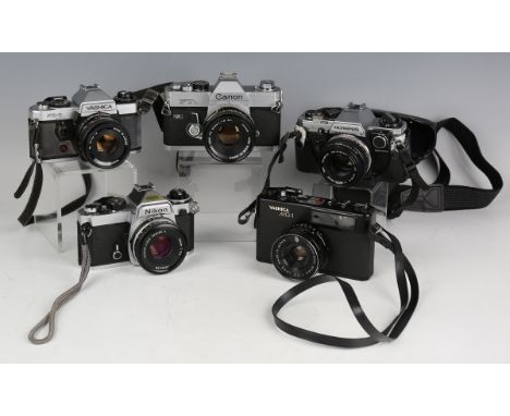 A collection of 35mm cameras and lenses, including an Olympus OM10 with Zuiko MC Auto-S 1:1.8 F=50mm lens, a Canon FT6 camera