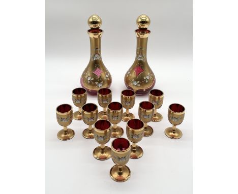 Two Murano ruby glass decanters with twelve matched goblets all decorated with gilt detail and flower reliefs