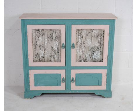 A painted pink and blue bookcase with wire fitted to the cupboard doors, with cupboard below on bracket feet, 107 cm wide, 33