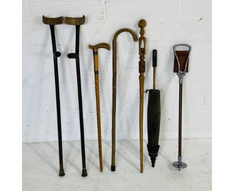 Three vintage wooden walking sticks including a tribal style stick, along with a pair of crutches, shooting stick, parasol et