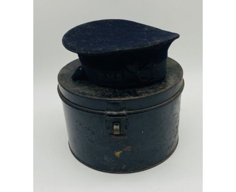 A navy blue sailors hat of circular form with a ribbon banding reading H.M.S, stored in a metal storage trunk - inner diamete