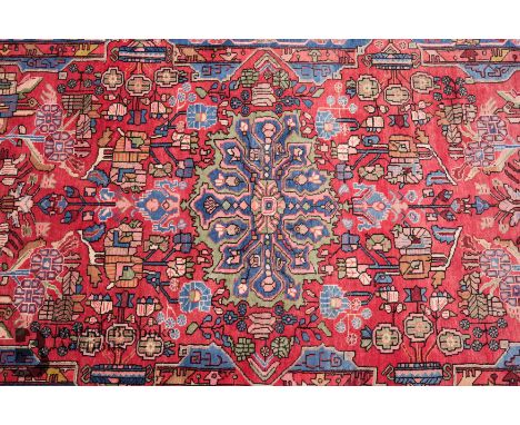 A Persian wool carpet, having a foliate border enclosing a field of flowers surround a central medallion, green, pink, red, b
