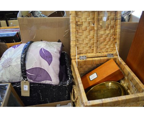 Two wicker baskets containing decorative cushions, a brass oval dish a wooden champagne box and a tablecloth.