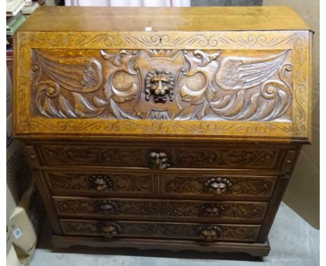 An early 20th Century oak Bureau carved with lion masks, birds, scrolls etc. with hinged fall with three long and two short d