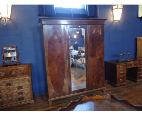An early 20th Century mahogany Wardrobe with stepped cornice and centre bevelled mirror panelled door flanked by a pair of ov
