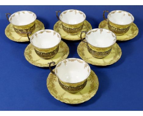 An Edwardian yellow and gilt set of six porcelain cups &amp; saucers with silver pierced and scrollwork cup holders, 6g 