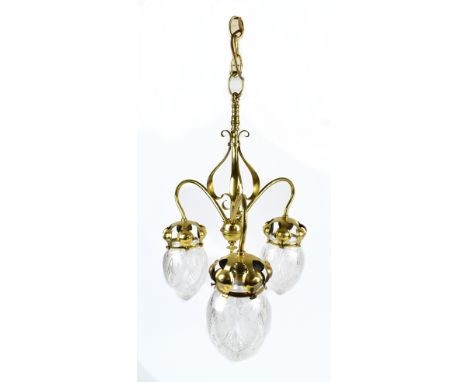 An Arts &amp; Crafts brass three branch ceiling light with scrolled detail and three clear glass etched shades, bearing regis