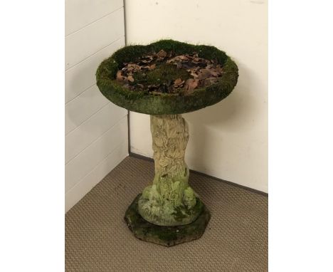 A weathered stone bird bath with tree trunk stem 