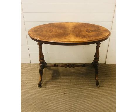 A small bur walnut effect oval table on a turned trestle frame with turned stretcher and carved supports on ivory ceramic cas