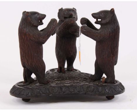 An early 20th century Black Forest carved wood model of three standing bears, on shaped conforming base, height 21.5cm