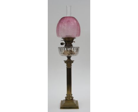 A Victorian brass corinthian column oil lamp, Evered's No.2 Patent, the pink glass shade etched with flowers, above a cut gla