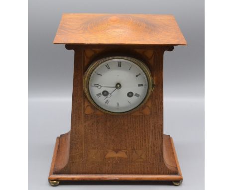 An Art Nouveau inlaid oak mantle clock, the domed top above a 9cm enamel dial with Roman numerals surrounded by inlaid stylis