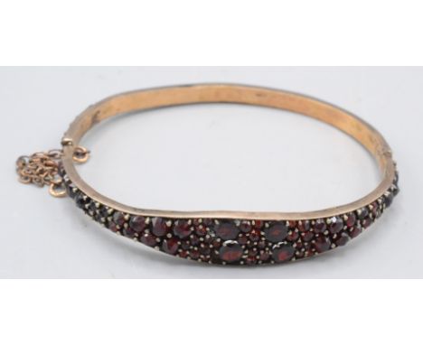 A low purity gold hinged bangle pave set with garnets.  Condition report: Clasp broken.