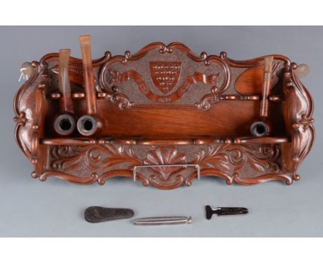 A carved oak pipe rack, early 20th century, the back inscribed 'One And All' beneath a shield showing the fifteen bezants of 