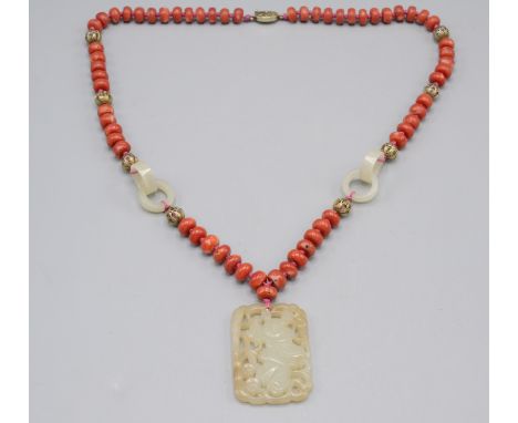 A Chinese carved jade pendant hanging from a red coral bead necklace with jade rings and filigree balls. Condition report: Na