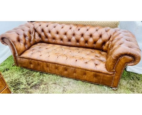 A 20th Century chesterfield tan leather sofa, scrolling back and arm rest, button back and button seated, raised on bun bowl 