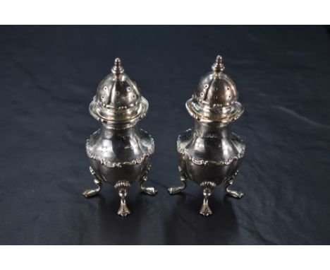 A pair of Edwardian cased silver pepperettes, of lobed urn-form, the domed, finial topped and pierced pull-off covers with mo