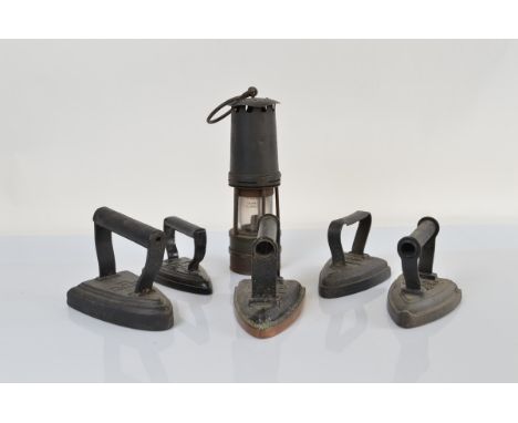 An early 20th Century brass and steel miners lamp, 27cm high and five early 20th Century flat irons