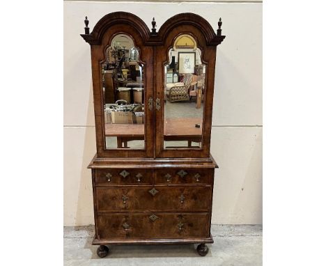 A Queen Anne walnut cabinet on chest, the double arch pediment with three urn finials over a pair of conforming doors with sh