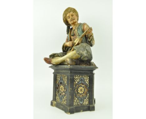 A vintage mid century hand painted German terracotta figurine of a Middle Eastern man. The figure modelled seated on hexagona