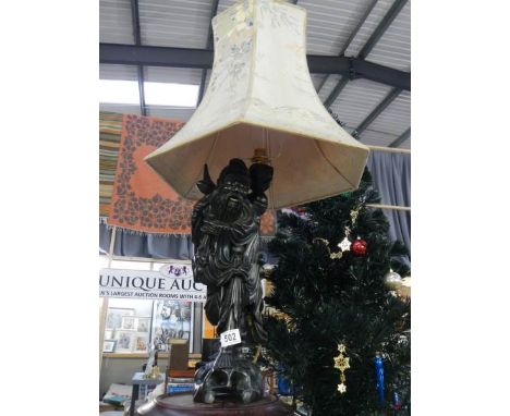 A carved wooden table lamp in the form of a Chinese gentleman complete with shade. 