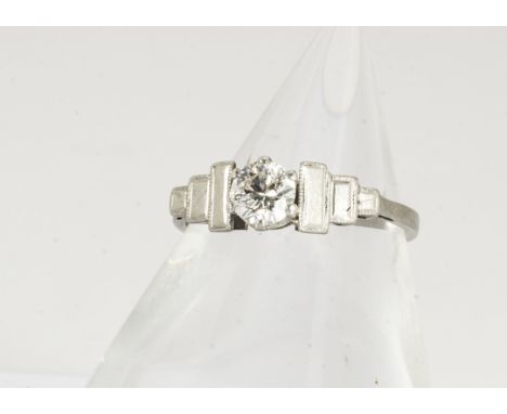 An Art Deco platinum diamond solitaire ring, the old cut diamond in claw setting having polished step cut shoulders, on a pla