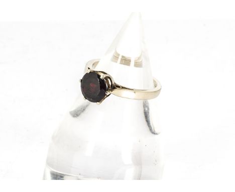 A continental yellow gold and garnet set dress ring, the red garnet claw set circular cut central stone on a yellow metal sha