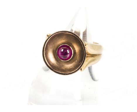 A modernist ruby and diamond yellow metal dress ring, the central cabochon ruby in disc top tablet with modern brilliant cut 