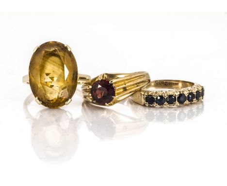 Three gem set rings, including a 9ct gold seven stone sapphire example, ring size O, a 9ct gold garnet signet ring, ring size