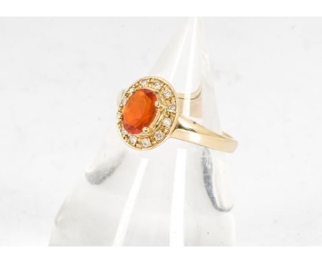 An 18 carat gold fire opal and diamond set cluster ring, the oval fire opal in four claw setting surrounded by a bezel of bri