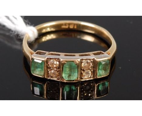 An Art Deco 18ct gold, emerald and diamond ring, arranged as three baguette cut emeralds each dispersed with two pavé set old