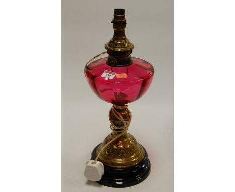A Victorian brass pedestal oil lamp having a cranberry glass reservoir (later converted), height 47cm (including fittings)