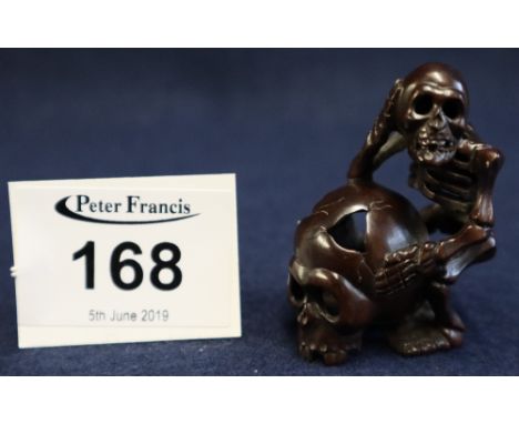 Japanese carved hardwood netsuke in the form of a skeleton leaning against a skull with inset mother of pearl signature panel