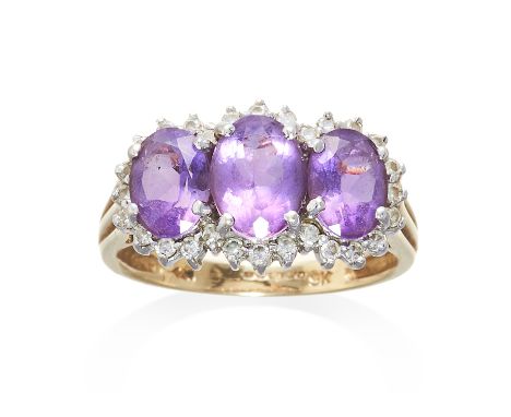 AN AMETHYST AND DIAMOND RING in 9ct yellow gold, comprising of three oval cut amethyst framed in round cut diamonds, stamped 