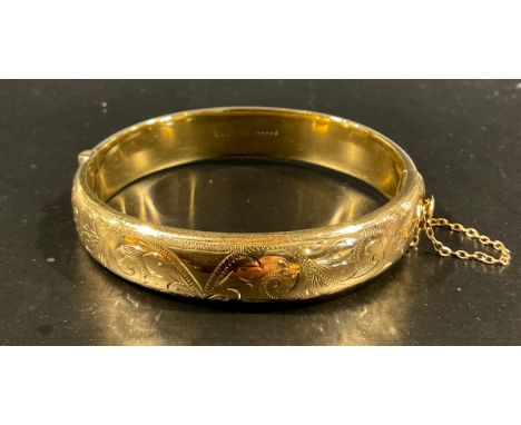 A 9ct gold patterned half hinged hollow bangle, with scroll decoration halfway round, measuring approx. 12mm wide, stamped "9