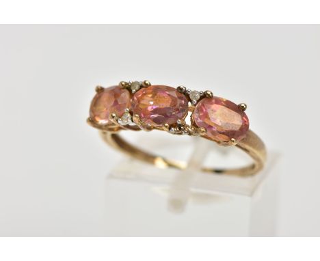 A YELLOW METAL GEM SET RING, designed with three oval cut mystic coated topaz, interspaced with single cut diamonds (one diam