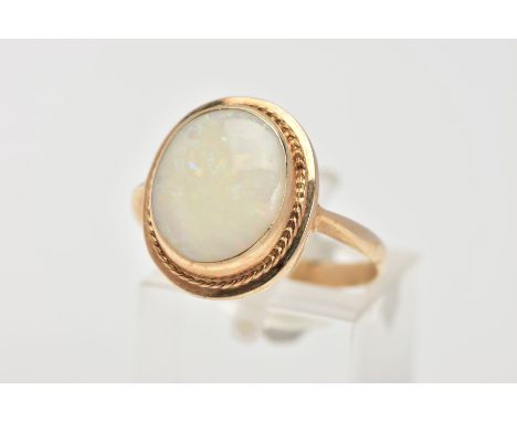 A YELLOW METAL OPAL RING, designed with an oval cut opal cabochon measuring approximately 13.9mm x 11.5mm, collet mount to a 