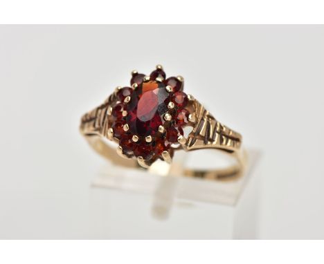 A 9CT GOLD GARNET CLUSTER RING, designed with a central oval cut garnet, within a surround of circular cut garnets, textured 