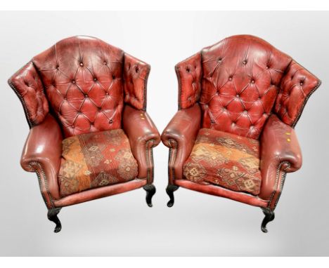 A pair of Chesterfield red button leather wingback armchairs on carved ebonised feet 