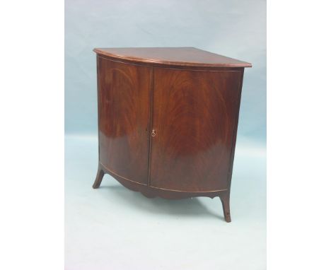 A late Georgian mahogany corner cupboard, bow-fronted with open shelves and tambour cupboard enclosed by a pair of flame-vene