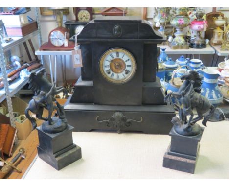 A large late Victorian black slate mantel clock, architectural form with applied masks, traditional dial and Ansonia gong-str