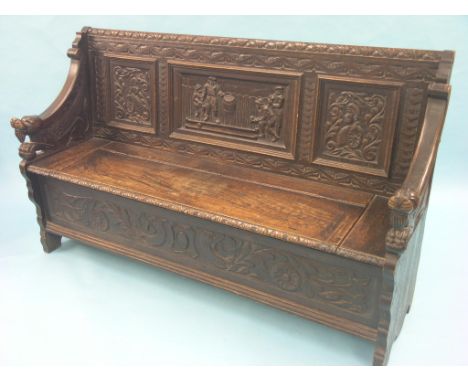 A Victorian Flemish-style dark oak settle, panelled back carved with male figures playing nine-pins, carved griffin arm-suppo