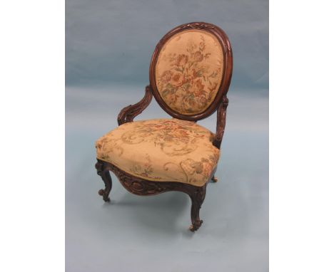 A Victorian mahogany spoon-back elbow chair, frame deeply-carved, on front cabriole legs with ceramic casters, upholstered se