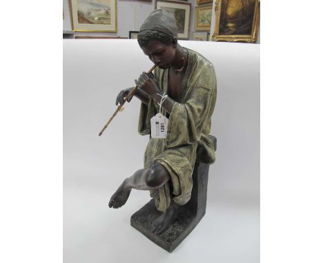 A Goldscheider Polychrome Painted Terracotta Figure of a Boy, seated on a pillar playing the flute wearing a loose-fitting to