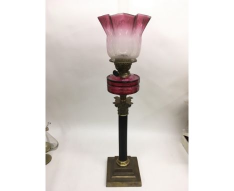 A brass Corinthian column oil lamp with cranberry glass reservoir and shade.