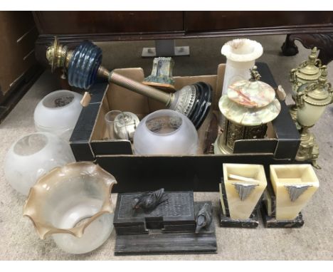 Two boxes containing a collection of oddments comprising clock garnitures, oil lamp, glass shades etc.