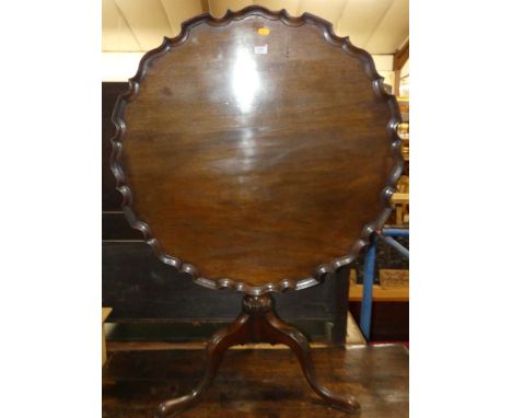 A George III mahogany pedestal tripod table having a circular dish top with pie crust rim to a gun barrel turned and carved p